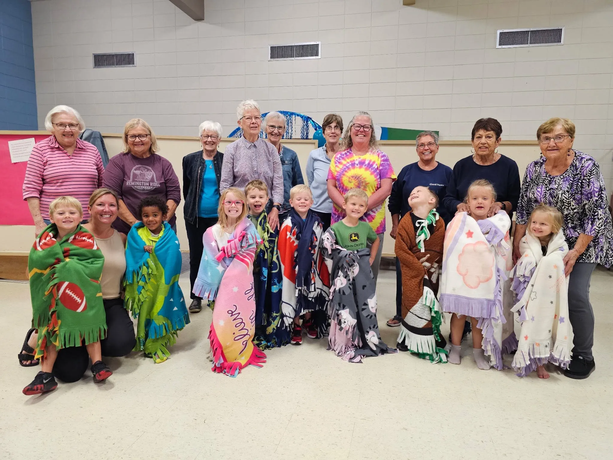 Little Blessings preschoolers wrapped in handmade fleece blankets alongside the church volunteers who made them