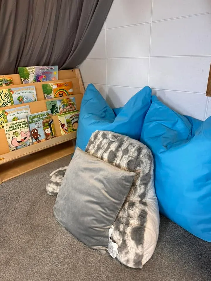 A cozy classroom reading nook with beanbags, soft pillows, and a picture-book display