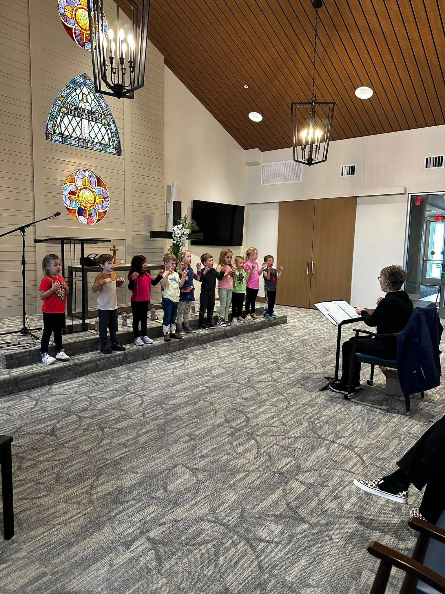 Preschoolers singing together at the front of the church sanctuary beneath the stained-glass windows