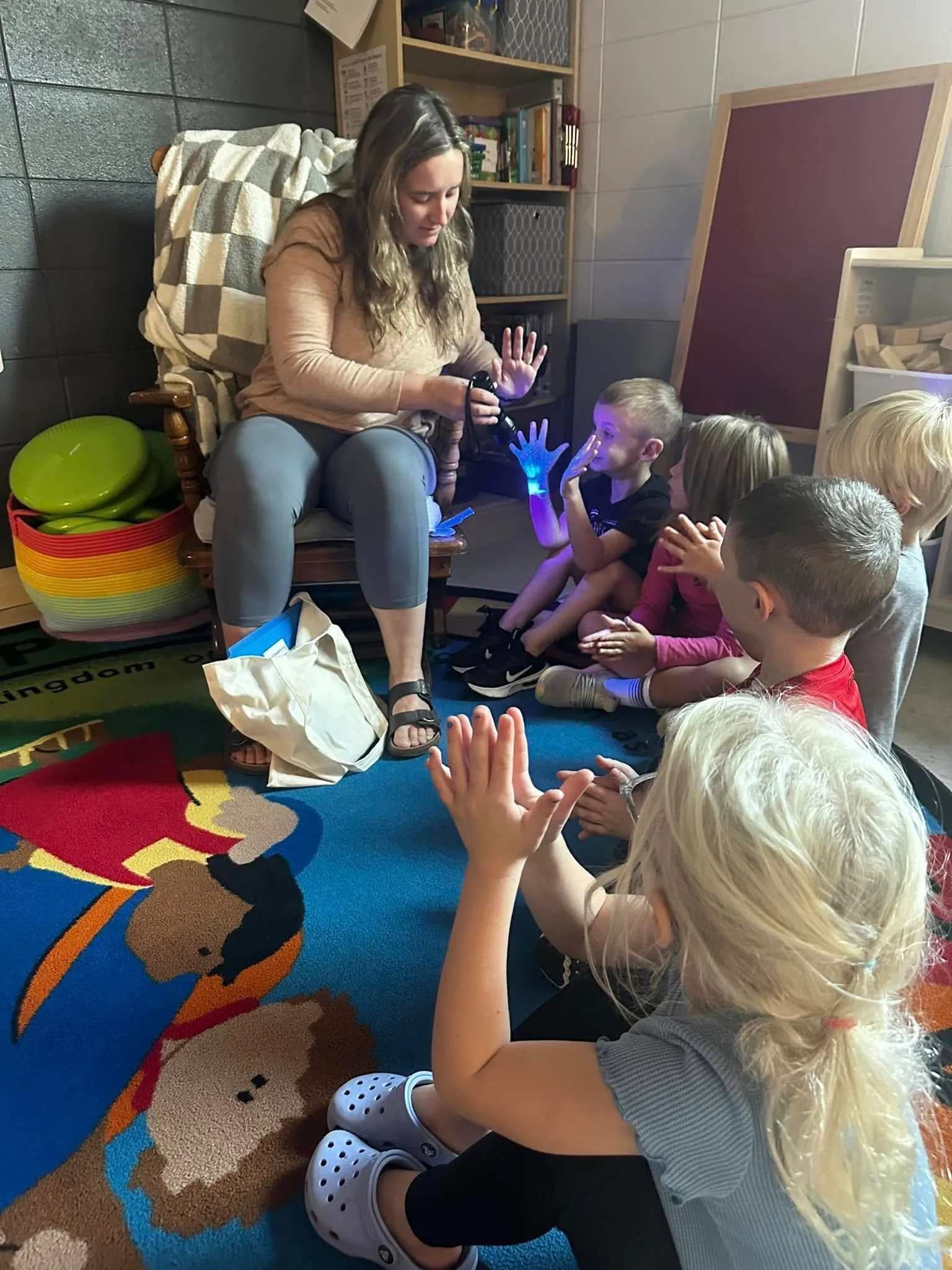 A teacher leads a hands-on glow-in-the-dark science activity with a circle of preschoolers